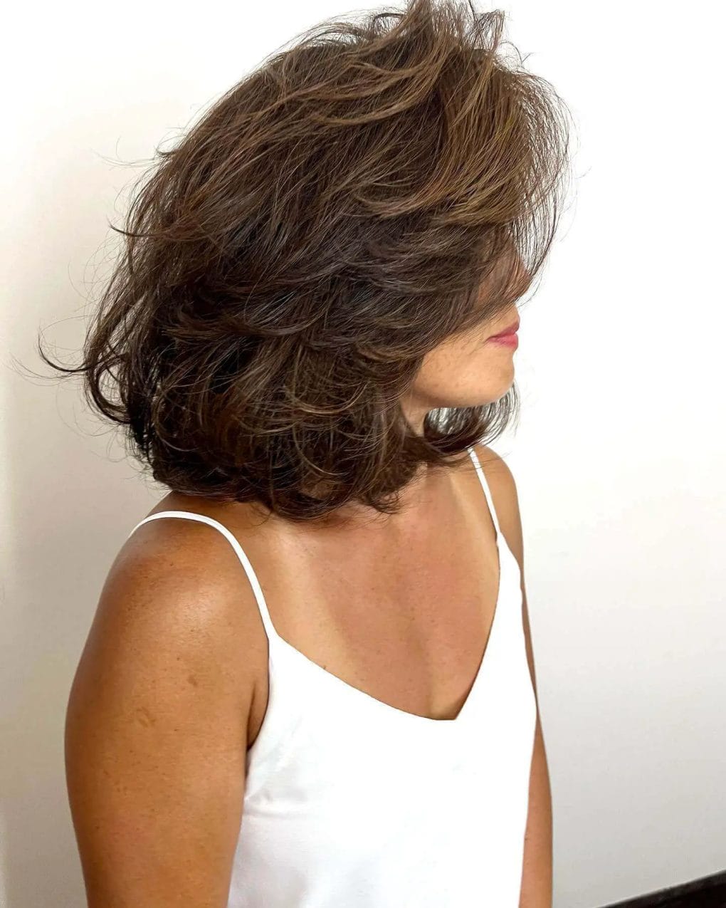 Voluminous tousled layered bob in warm brunette with subtle highlights.