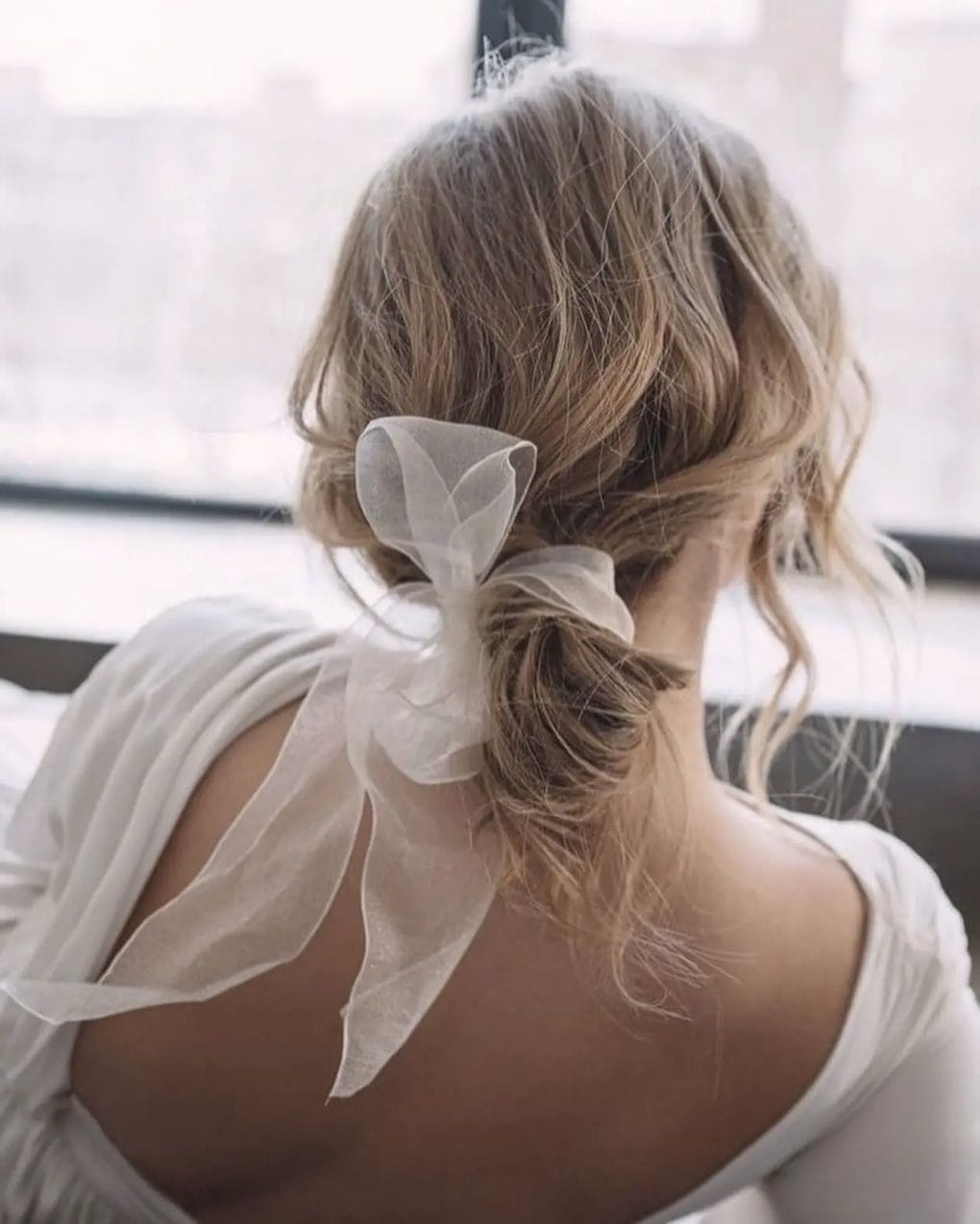 Tousled low bun with strands loosely pulled back and an organza bow