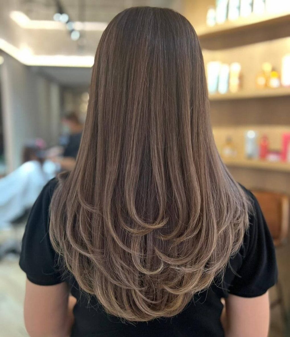 Cascading U-shaped cut with 3D layers and balayage touches on a brunette base.