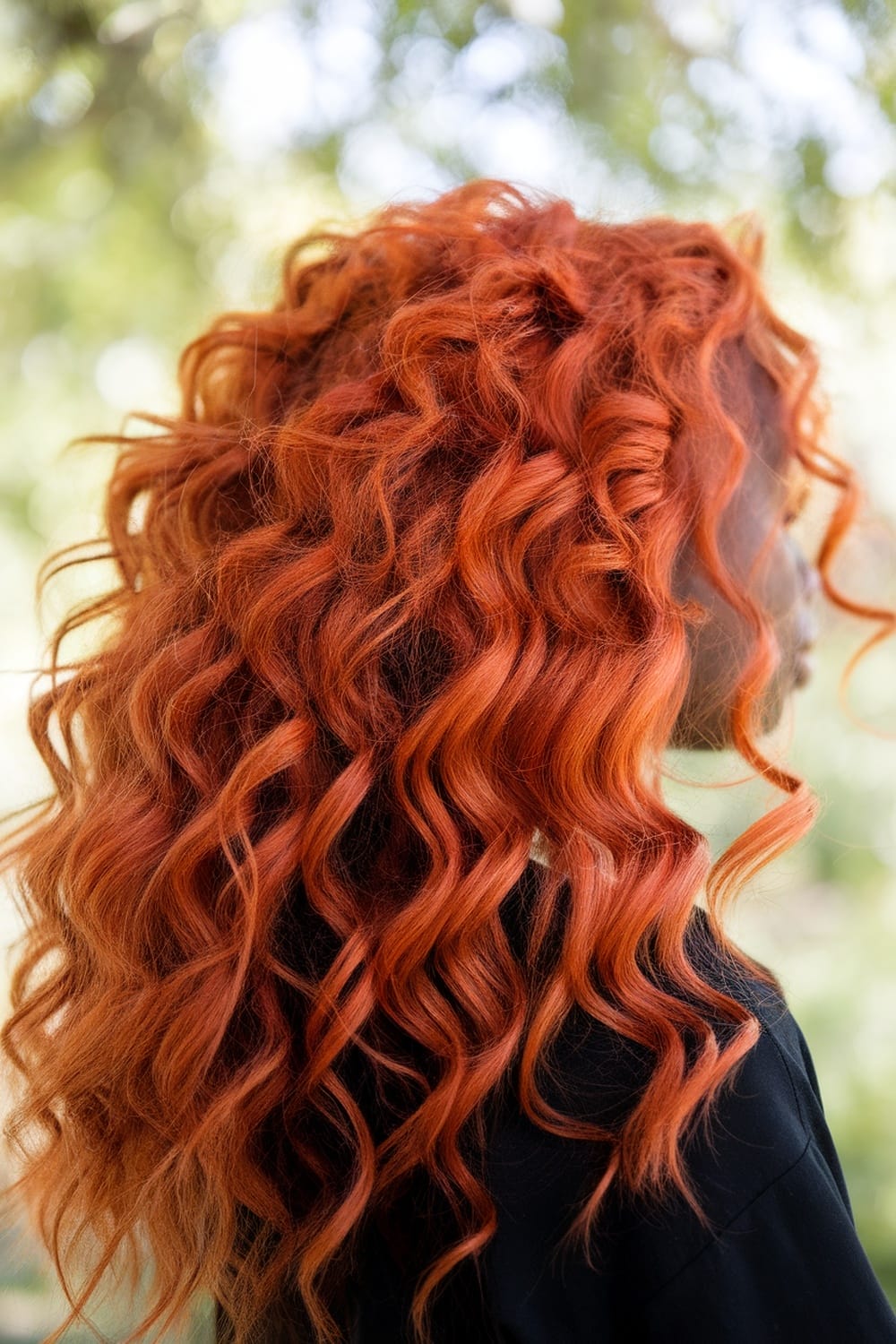 A woman with vibrant copper curls, standing outdoors with a blurred background.