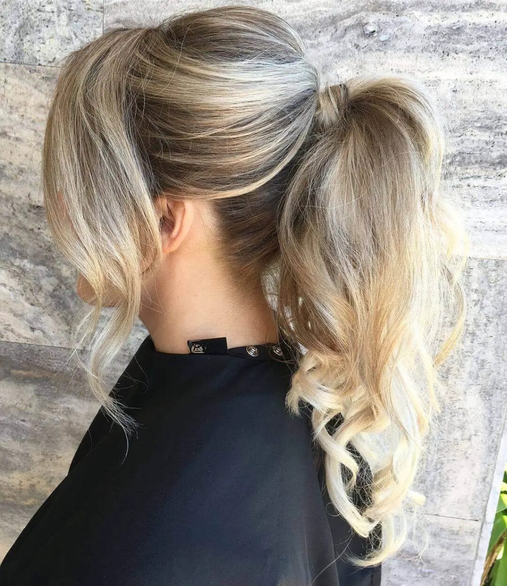 Voluminous curly ash blonde ponytail with darker roots, showcasing romantic curls and expert highlights.