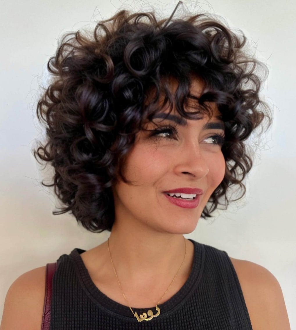 Voluminous curly bob with espresso base and wispy bangs.