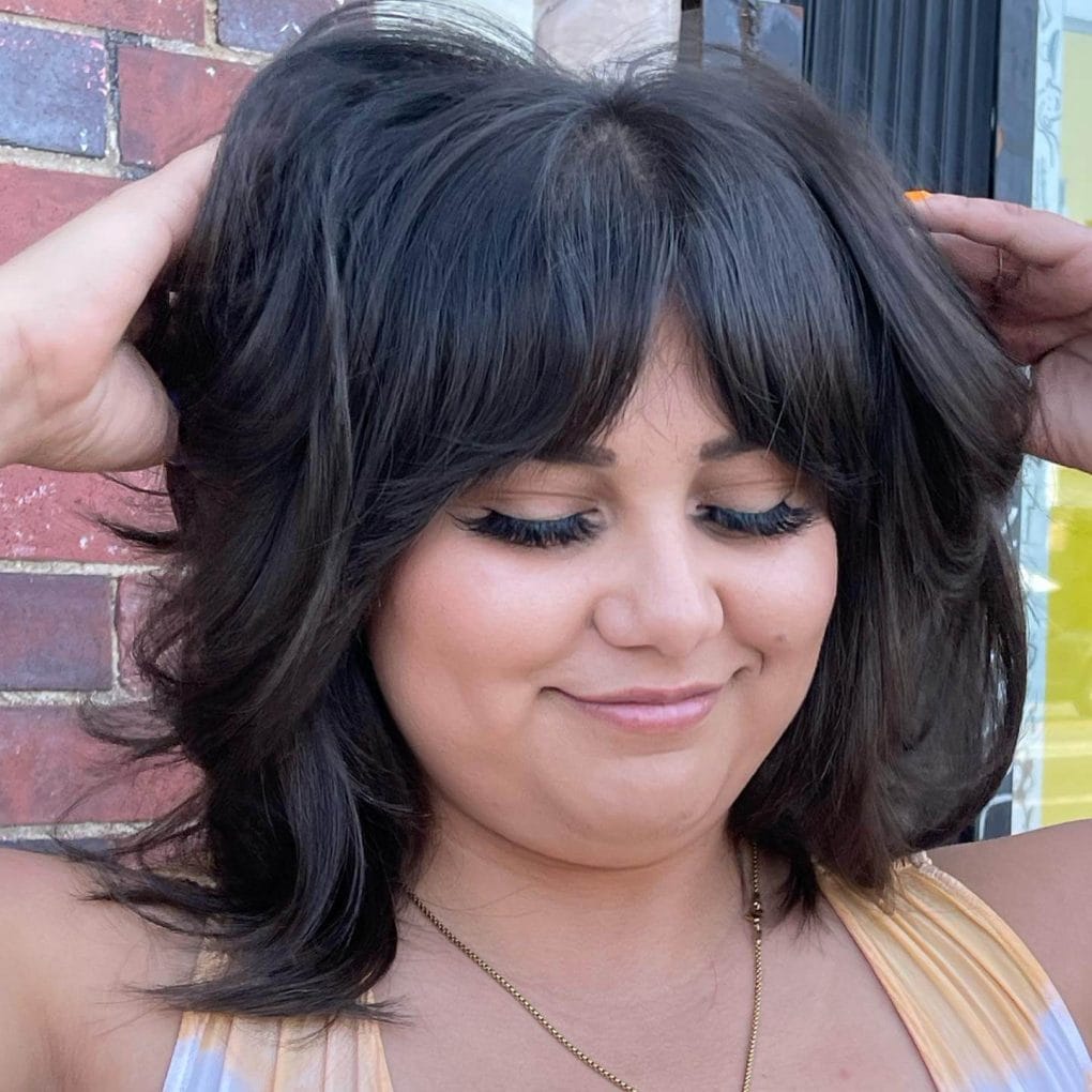 Dark voluminous waves complemented with youthful curtain bangs, enhancing facial features and volume.