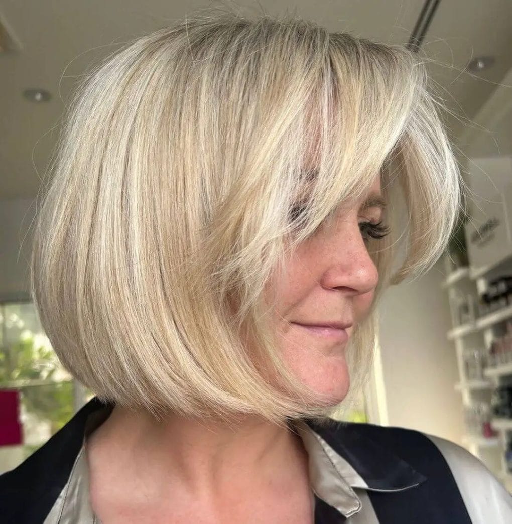 Voluminous layered bob with soft curtain bangs and textured blonde highlights.