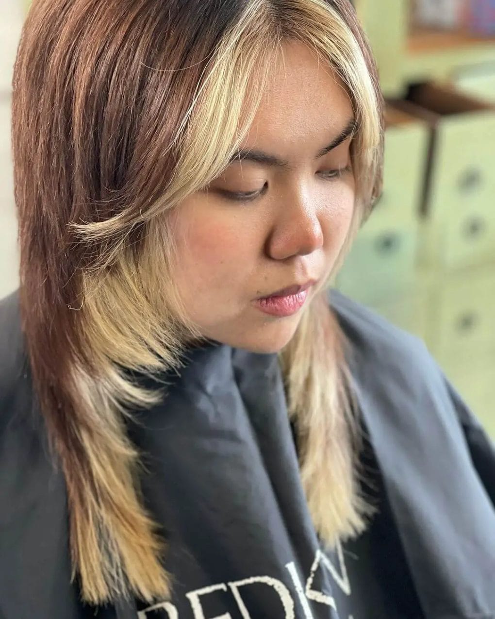 Soft layered jellyfish hairstyle transitioning from warm brown to sandy blonde ombre with a side part and slight curl.
