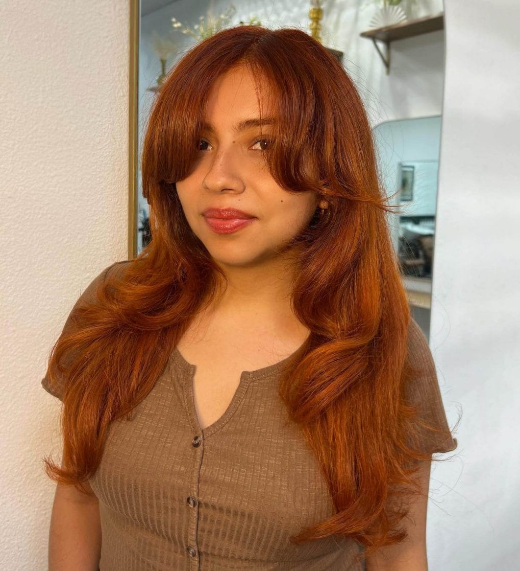 Warm copper hair with soft fringe, long layers, and curled ends.