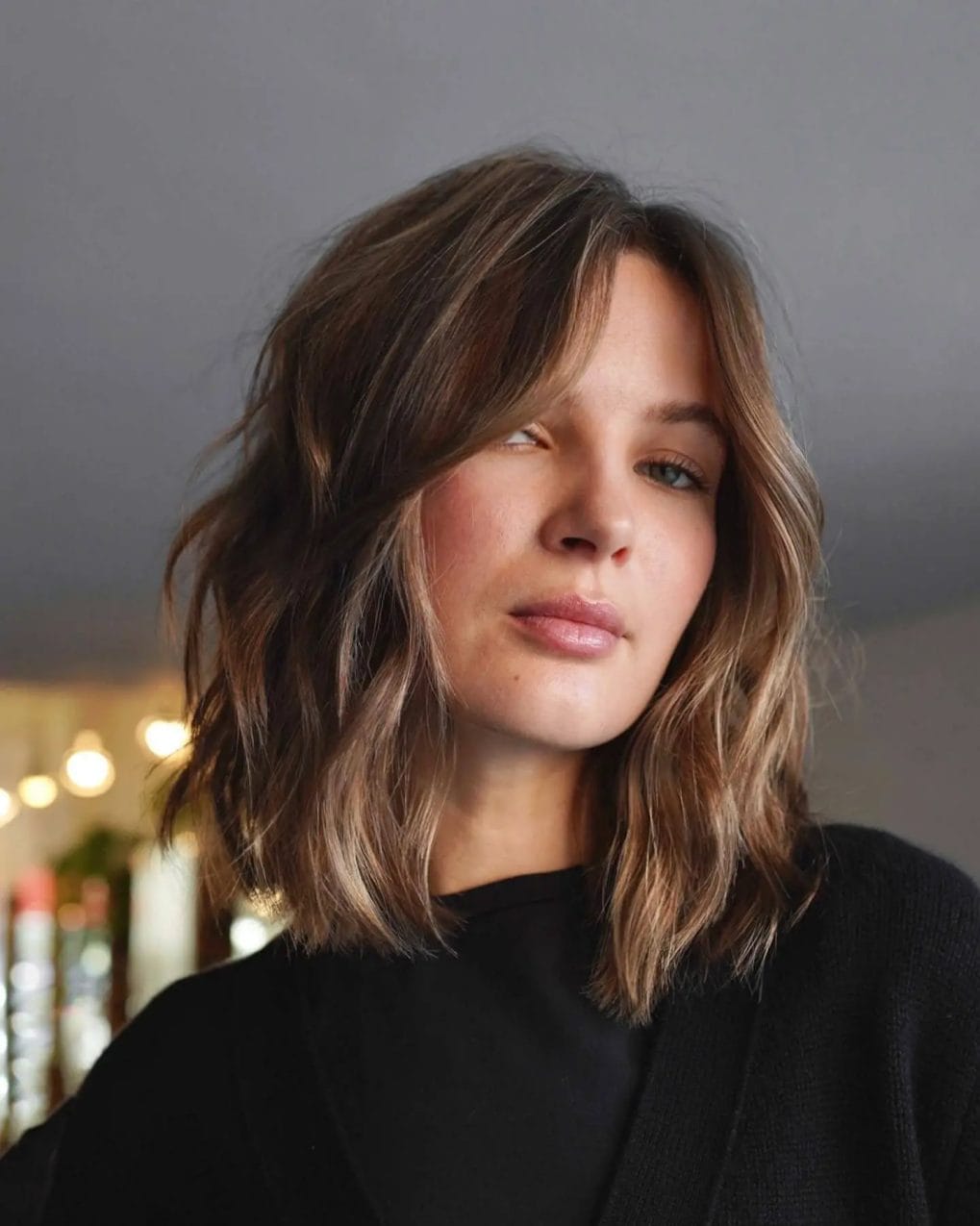 Wavy lob with sun-kissed balayage and perfectly styled curtain bangs.