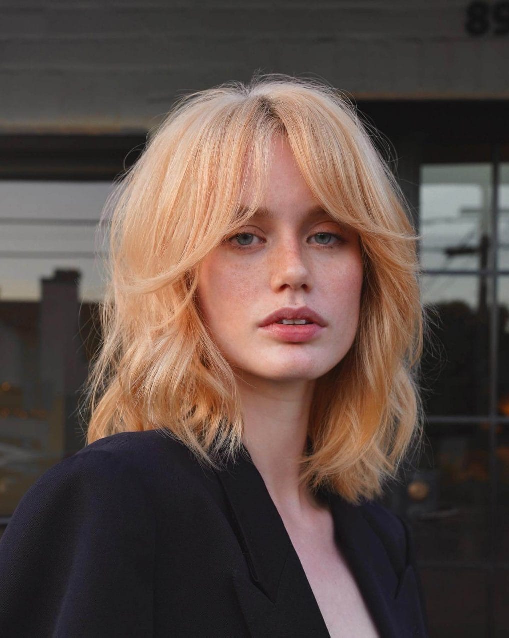 Tousled medium wheat-blonde shaggy lob with airy curtain bangs around cheekbones.