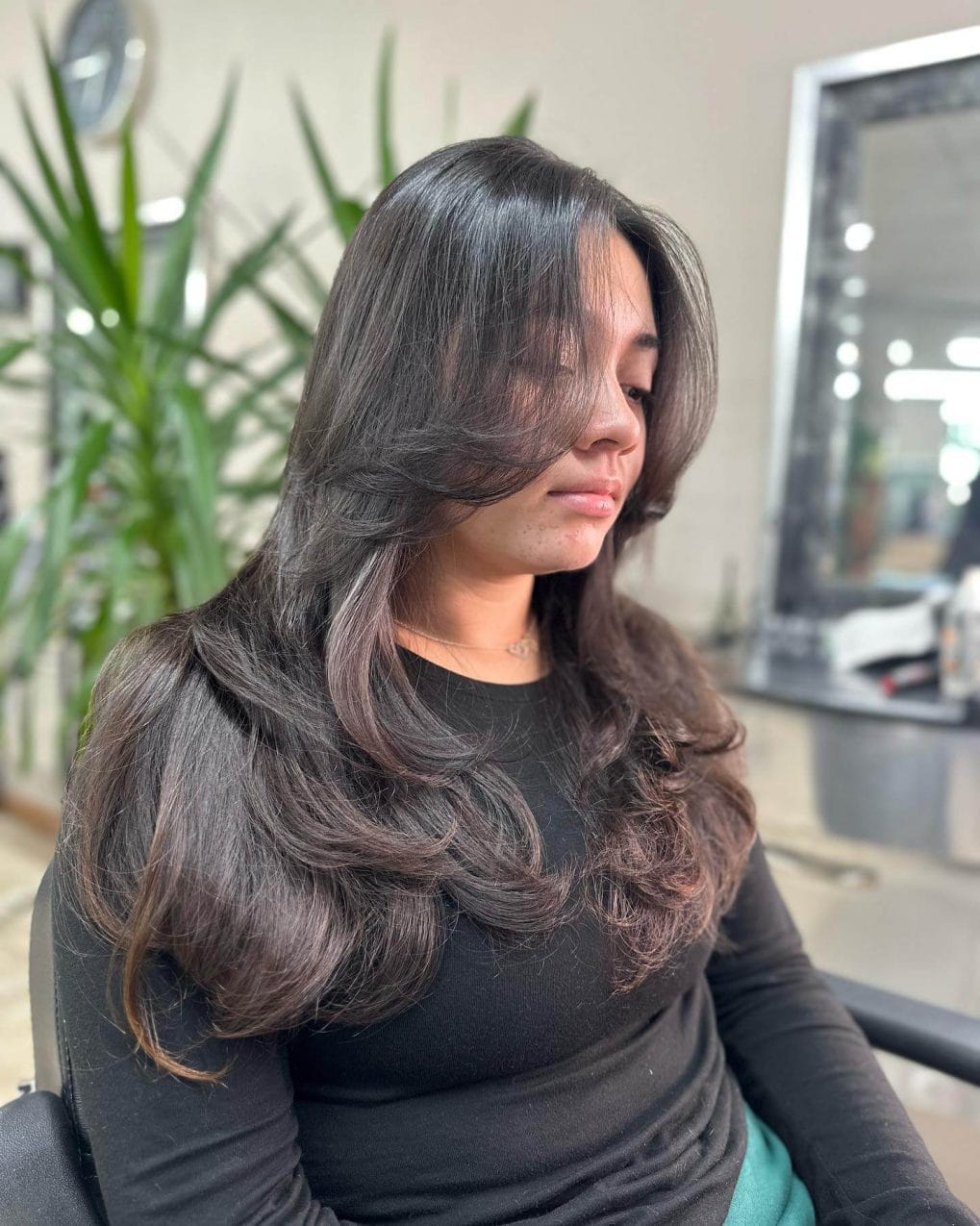 Layered Butterfly Cut on dark hair complemented by bold curtain bangs.