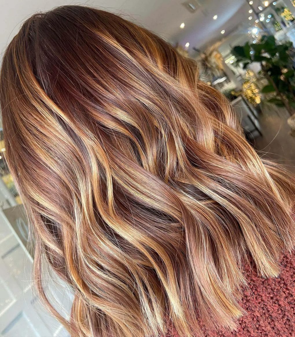 Wavy balayage hairstyle with warm honey and caramel tones, evoking a cozy winter atmosphere.