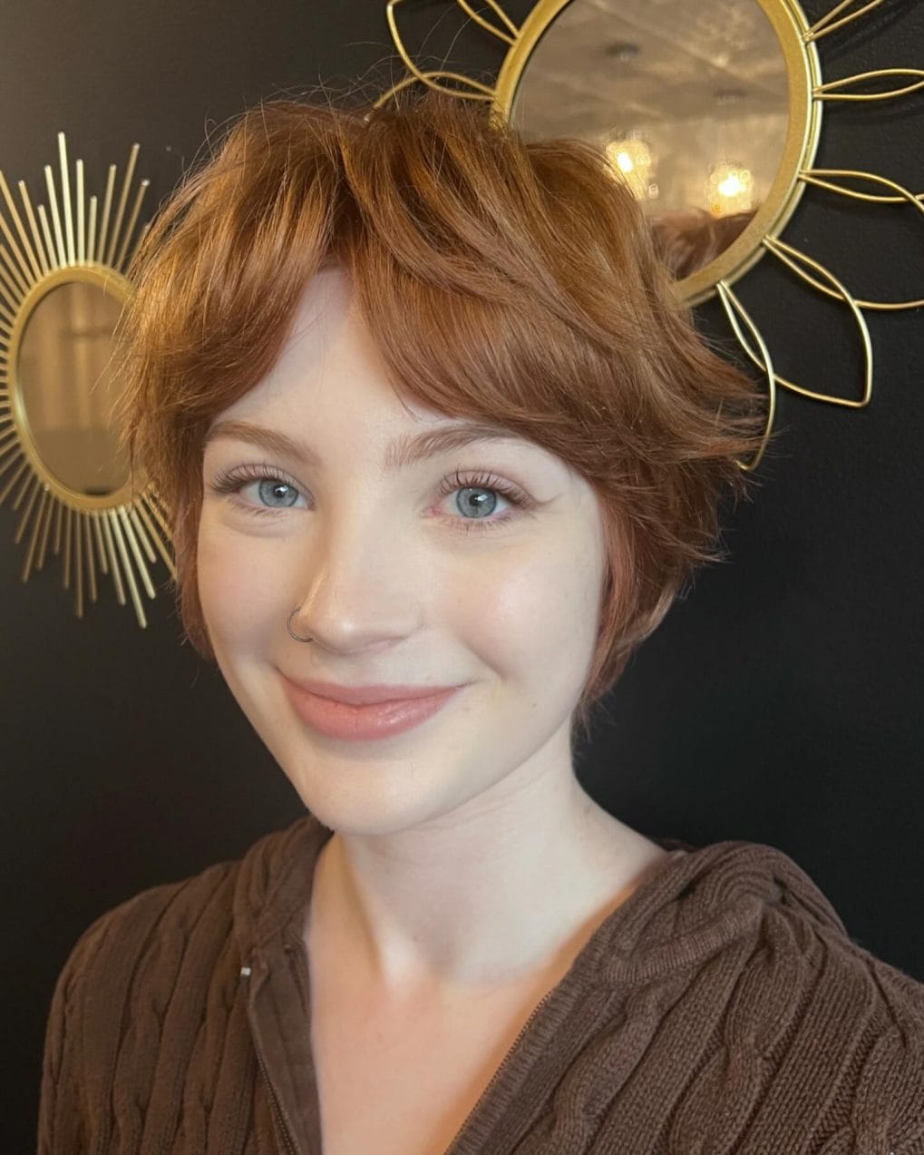 Soft copper pixie cut with delicate layers and wispy light bangs highlighting bright eyes