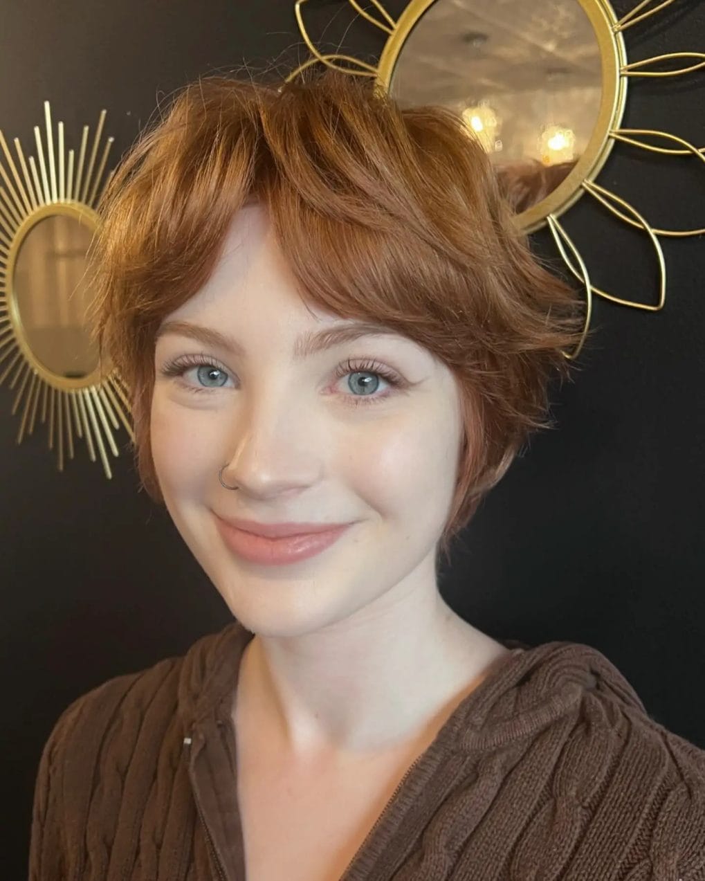 Soft copper pixie cut with delicate layers and wispy light bangs highlighting bright eyes